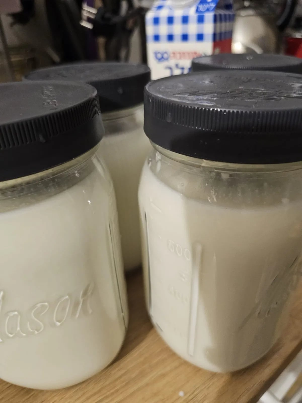 Two Mason jars of thick, creamy finished yogurt beside a carton of milk